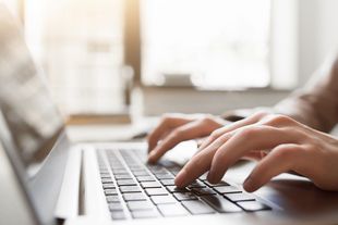 Zwei Hände tippen auf der Tastatur eines Laptops.