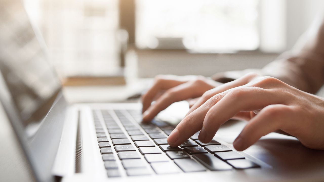 Zwei Hände tippen auf der Tastatur eines Laptops.