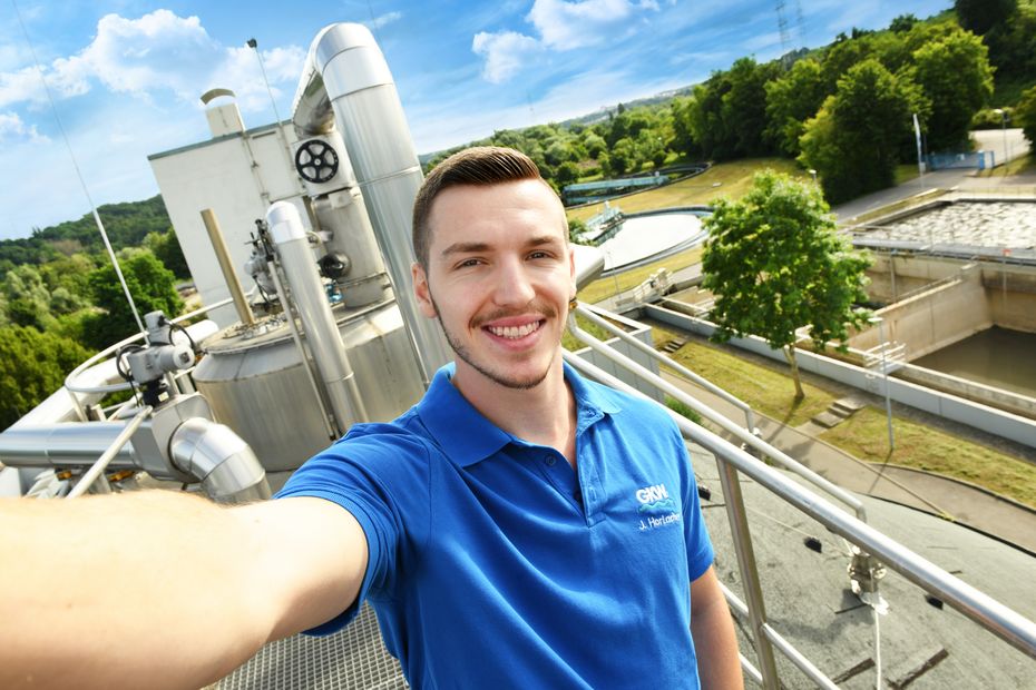 Ein Auszubildender der ein Selfie macht, im Hintergrund ist die Kläranlage zu sehen.